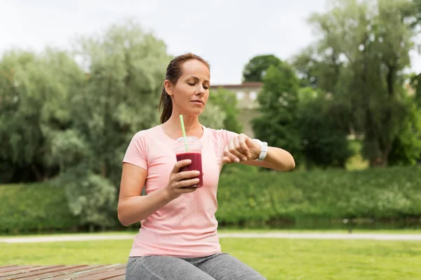 Vrouw met shake kijken naar slimme horloge in park — Stockfoto