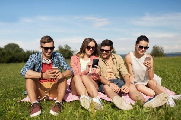 Χαμόγελο φίλοι με smartphones που κάθεται στο γρασίδι — Φωτογραφία Αρχείου