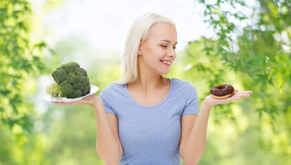 Smiling woman with broccoli and donut — Stock Photo, Image