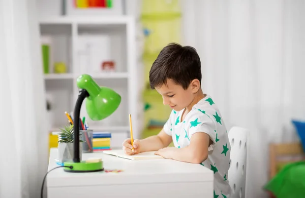 Маленький мальчик пишет записную книжку дома — стоковое фото