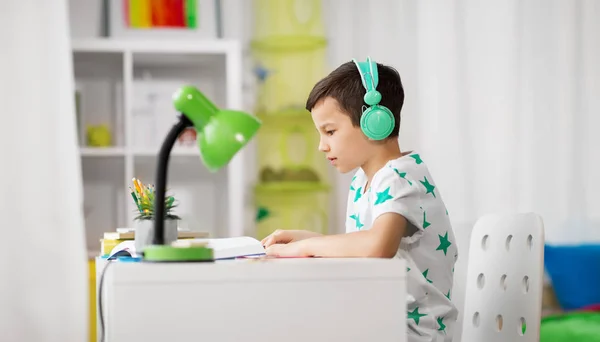 Student pojke i hörlurar läser bok hemma — Stockfoto