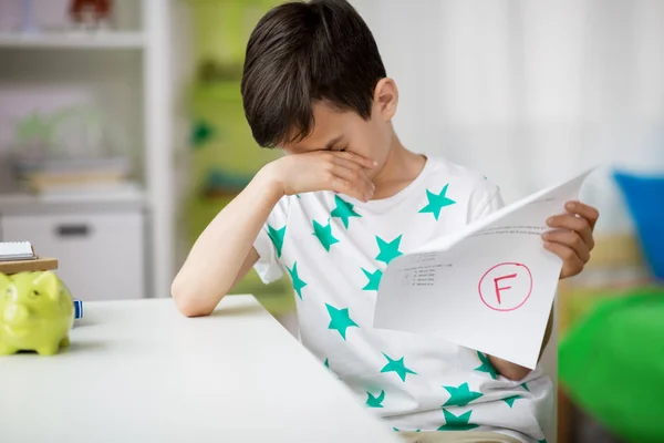 Menino triste segurando teste escolar com nota f — Fotografia de Stock