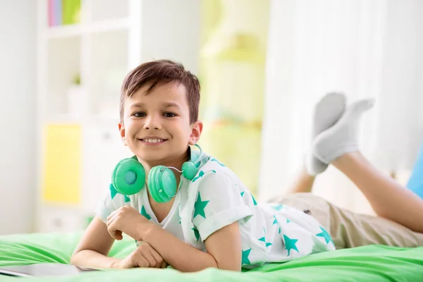 Leende pojke med hörlurar och TabletPC hemma — Stockfoto