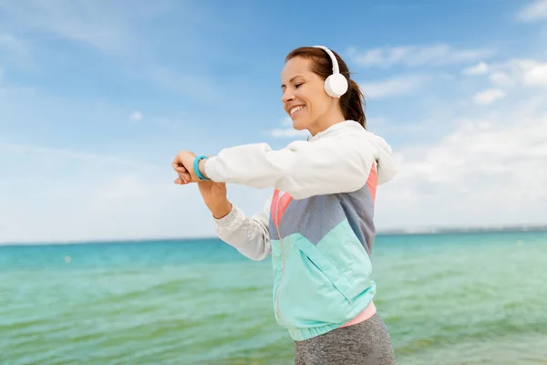 Frau mit Kopfhörer und Fitness-Tracker am Strand — Stockfoto