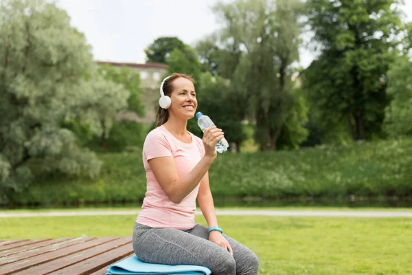 Mujer en auriculares agua potable en el parque — Foto de Stock
