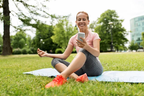 Mulher com smartphone descansando no tapete no parque — Fotografia de Stock