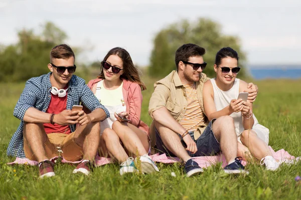 Lachende vrienden met smartphones zitten op gras — Stockfoto