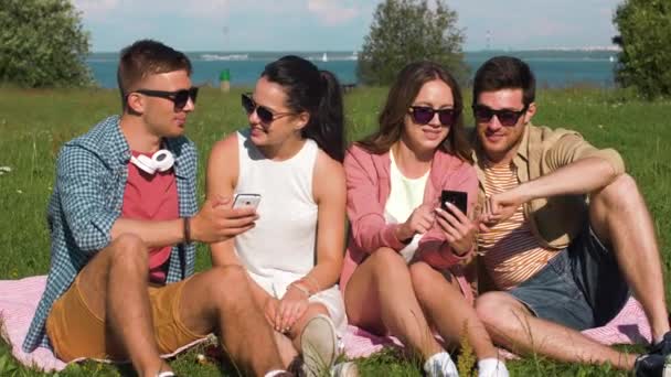 Amici sorridenti con smartphone seduti sull'erba — Video Stock