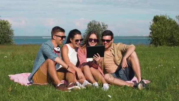 Amigos sonrientes con tableta pc sentado en la hierba — Vídeo de stock