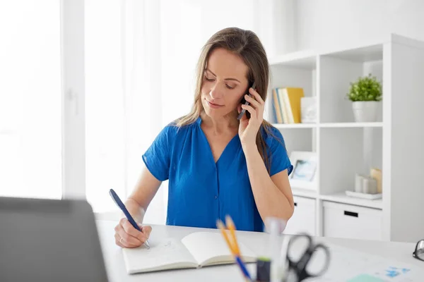 Woman with notepad calling on smartphone at office — Stock Photo, Image