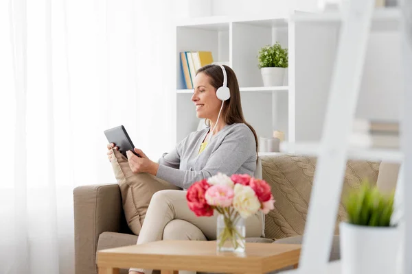 Femme heureuse avec tablette PC et écouteurs à la maison — Photo