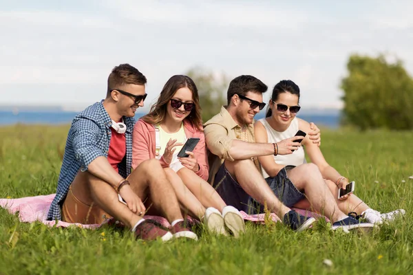 Amigos sonrientes con teléfonos inteligentes sentados en la hierba —  Fotos de Stock