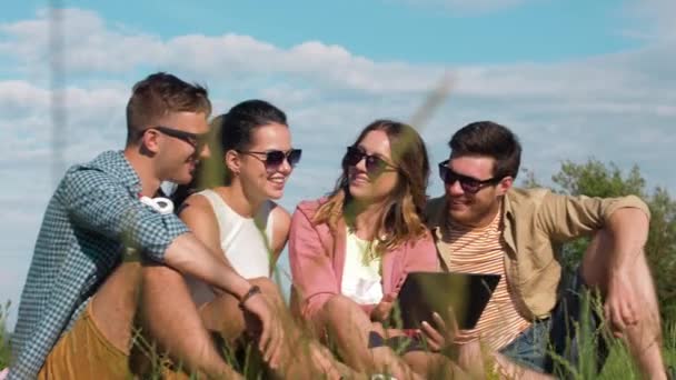 Amigos sonrientes con tableta pc sentado en la hierba — Vídeos de Stock