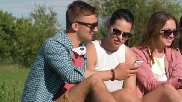 Amigos sonrientes con teléfonos inteligentes en el parque de verano — Vídeos de Stock