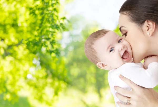Mother kissing baby over green natural background — Stock Photo, Image