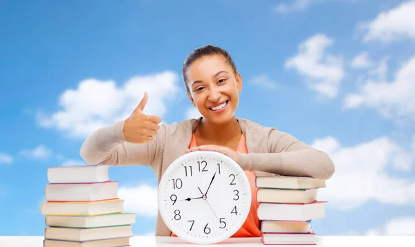 Estudiante con libros y reloj mostrando pulgares hacia arriba —  Fotos de Stock