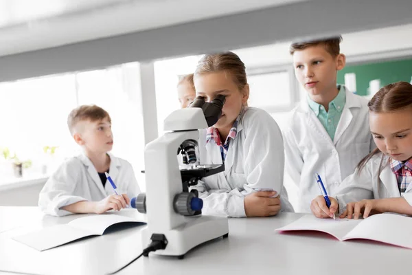 Niños o estudiantes con biología de microscopio en la escuela — Foto de Stock