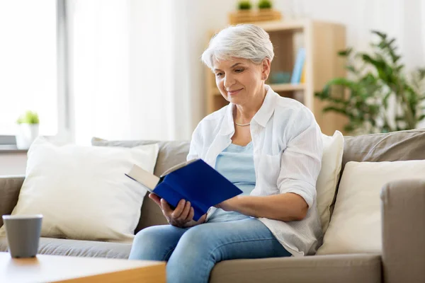 Szczęśliwy uśmiechający się starszy kobieta czytania książki w domu — Zdjęcie stockowe