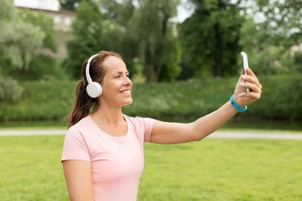 Mujer en los teléfonos toma selfie por teléfono inteligente en el parque — Foto de Stock