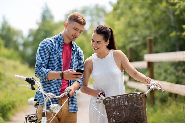 Пара с велосипедами и смартфоном летом — стоковое фото