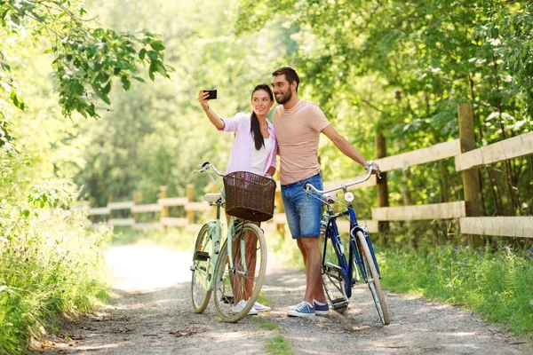 Пара с велосипедами делает селфи на смартфоне — стоковое фото