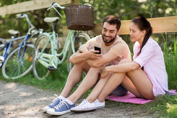 Pareja con smartphone y bicicletas en el parque de verano —  Fotos de Stock