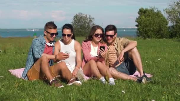 Smiling friends with smartphones sitting on grass — Stock Video