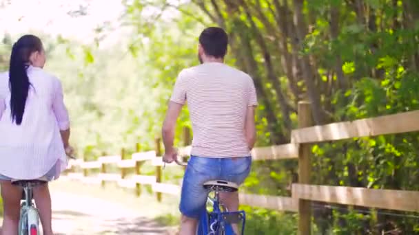 Feliz pareja montando bicicletas en el parque de verano — Vídeos de Stock