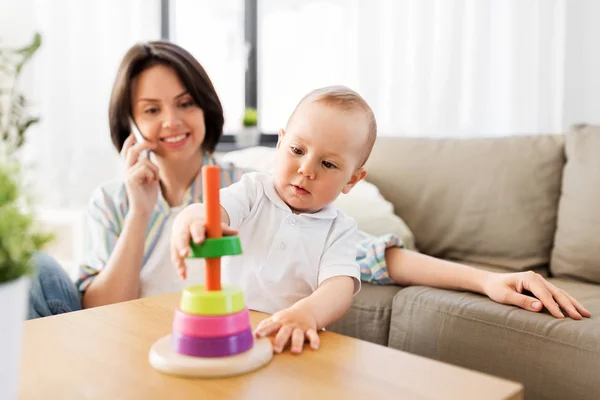Bebé niño jugando juguete y madre llamando por teléfono —  Fotos de Stock