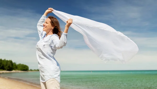 Gelukkige vrouw met sjaal wuiven in de wind op strand — Stockfoto