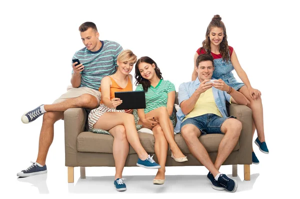 Amigos con tablet PC y teléfonos inteligentes se sientan en el sofá — Foto de Stock