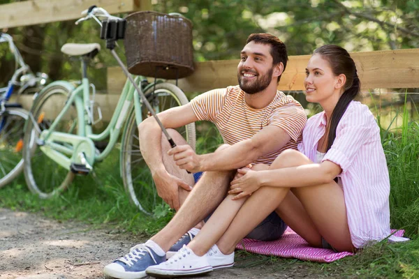 ライフ スタイル コンセプト 自転車の夏の公園で Selfie スティック スマート フォンで写真を撮ると幸せなカップル — ストック写真
