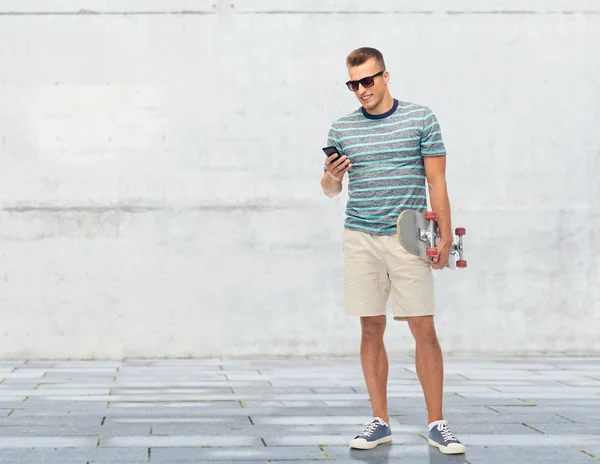 Smiling young man with skateboard and smartphone — Stock Photo, Image
