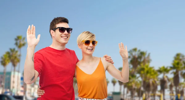 Paar in zonnebril knuffelen en handen zwaaien — Stockfoto