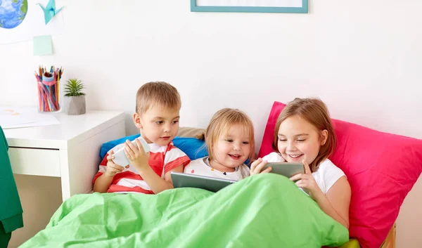 Crianças com tablet pc e smartphones na cama em casa — Fotografia de Stock