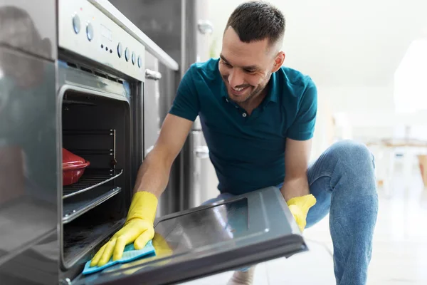 Man with rag cleaning oven door at home kitchen — Stock Photo, Image