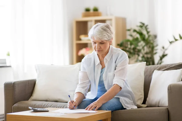 Senior woman with papers and calculator at home — Stock Photo, Image