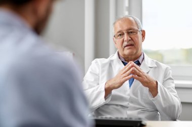 senior doctor talking to male patient at hospital clipart
