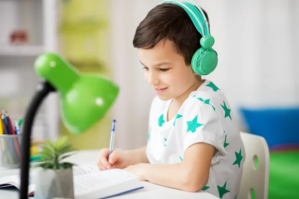 Chlapec ve sluchátkách s učebnicovým učením doma — Stock fotografie