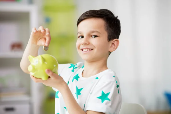 Little boy putting coin into piggy bank at home — Stock Photo, Image
