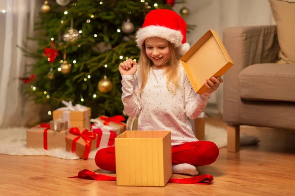 Menina animado em santa chapéu abrir presente de Natal — Fotografia de Stock