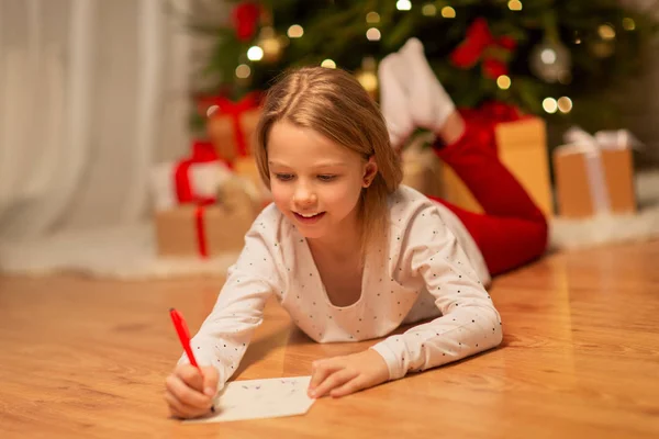 自宅でクリスマスの買い物リストを書いている女の子を笑顔 — ストック写真