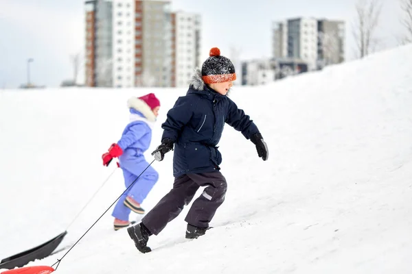 Crianças com trenós escalando neve colina no inverno — Fotografia de Stock