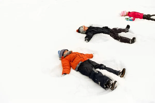 Bambini felici che fanno angeli di neve in inverno — Foto Stock