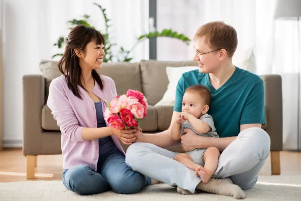 Glückliche Familie mit Blumen und Baby zu Hause — Stockfoto