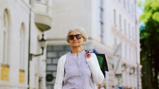 Mujer mayor con bolsas de compras caminando en la ciudad — Vídeos de Stock