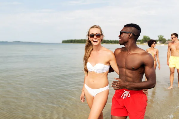 Pareja de raza mixta caminando a lo largo de la playa con amigos — Foto de Stock