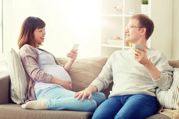 Mann und schwangere Frau mit Smartphone zu Hause — Stockfoto