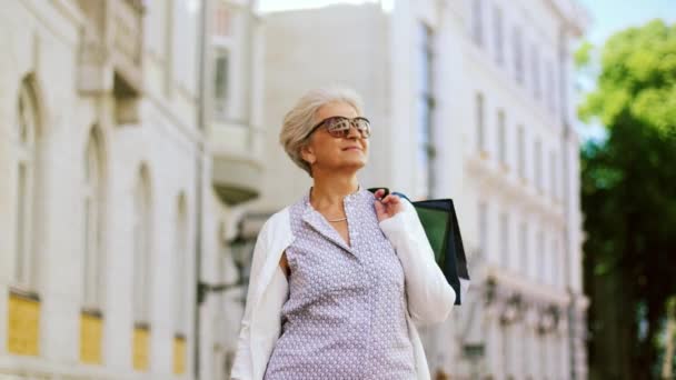 Senior vrouw met boodschappentassen, wandelen in de stad — Stockvideo