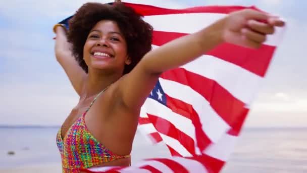 Mujer africana feliz con bandera americana en la playa — Vídeo de stock